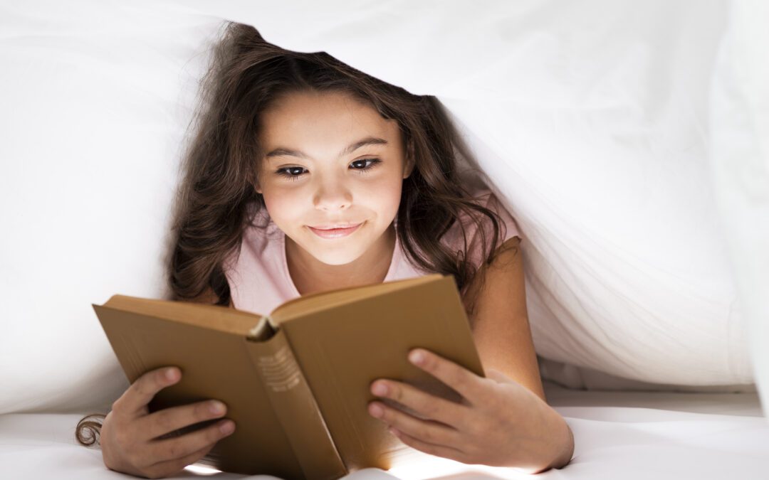 Young girl reading under the covers.
