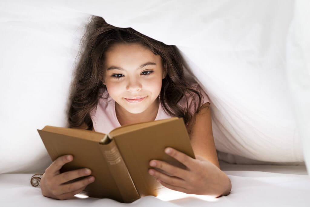 Young girl reading under the covers.